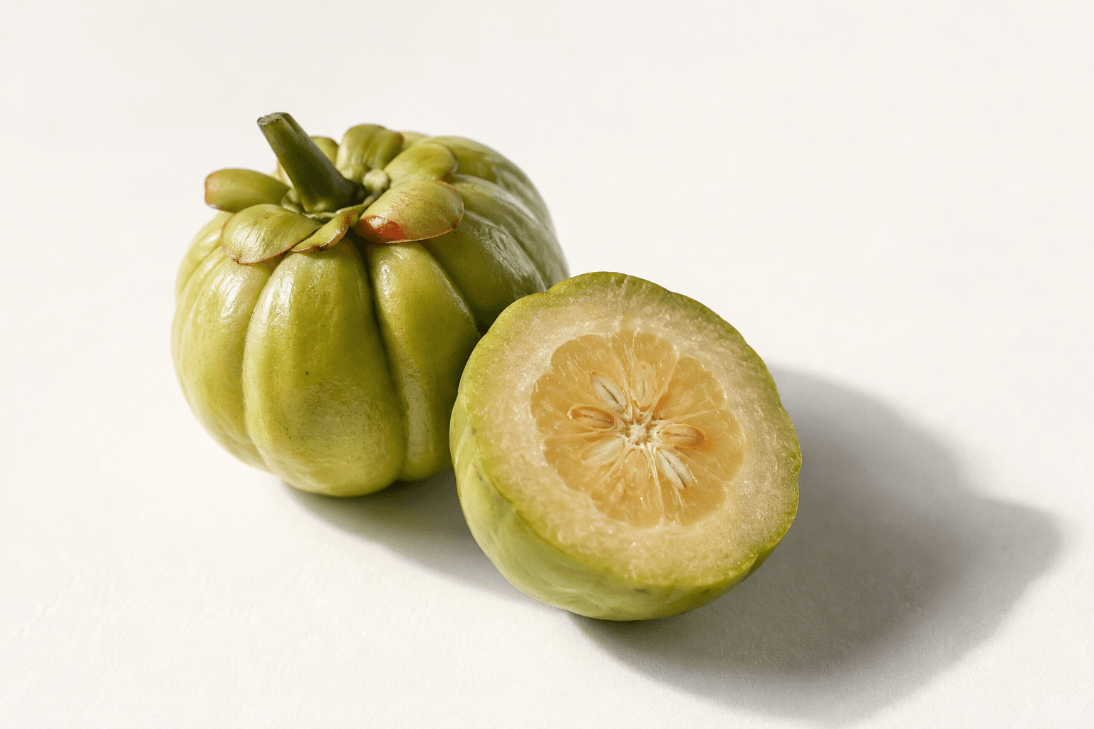 A whole Malabar tamarind fruit beside one cut in half, showing the pale interior